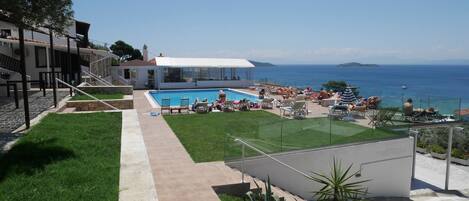 A pool area with a clear view of the sea, a covered seating area, and a pathway leading to the pool.