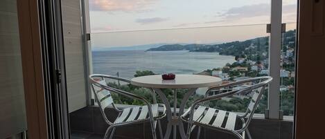 Un balcón con mesa y sillas, con vistas al litoral, casas y colinas.