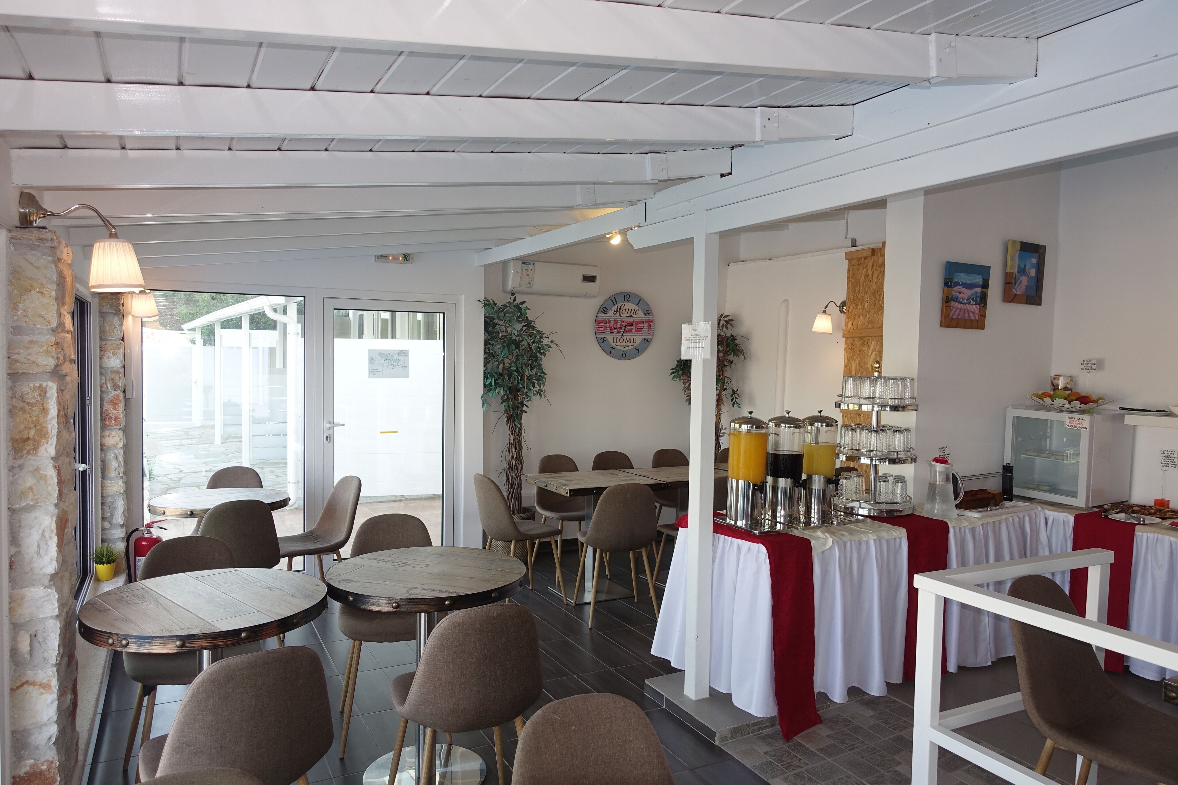 Un restaurant avec des tables et des chaises rondes, un espace buffet proposant des plats et des boissons, et une vue sur l’extérieur.