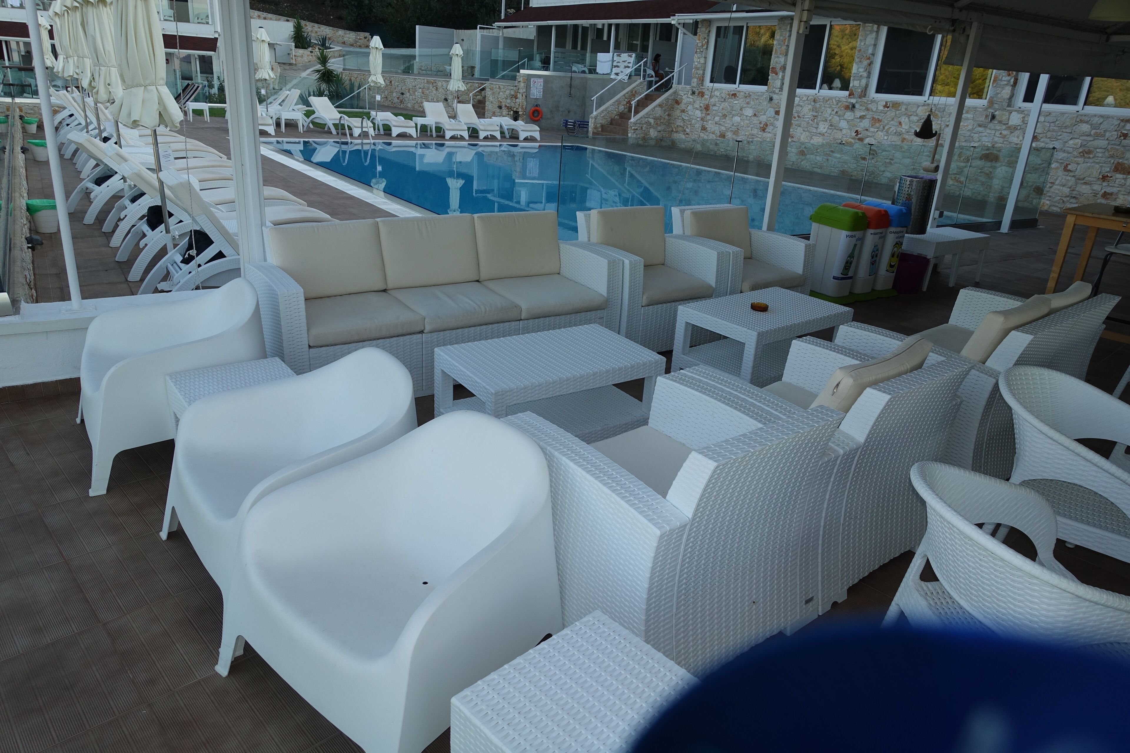 A poolside area with white wicker furniture, a swimming pool, and a stone wall backdrop.