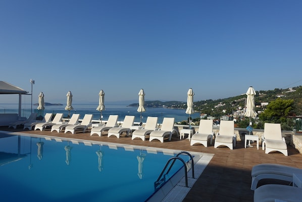 A poolside area with lounge chairs and umbrellas, overlooking a coastal landscape.