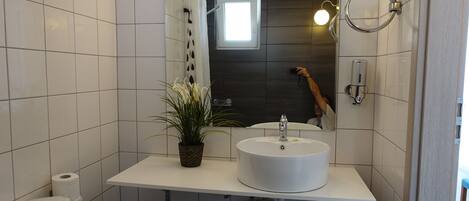 A modern bathroom with white tiles, a white sink, a potted plant, a toilet, and a mirror.