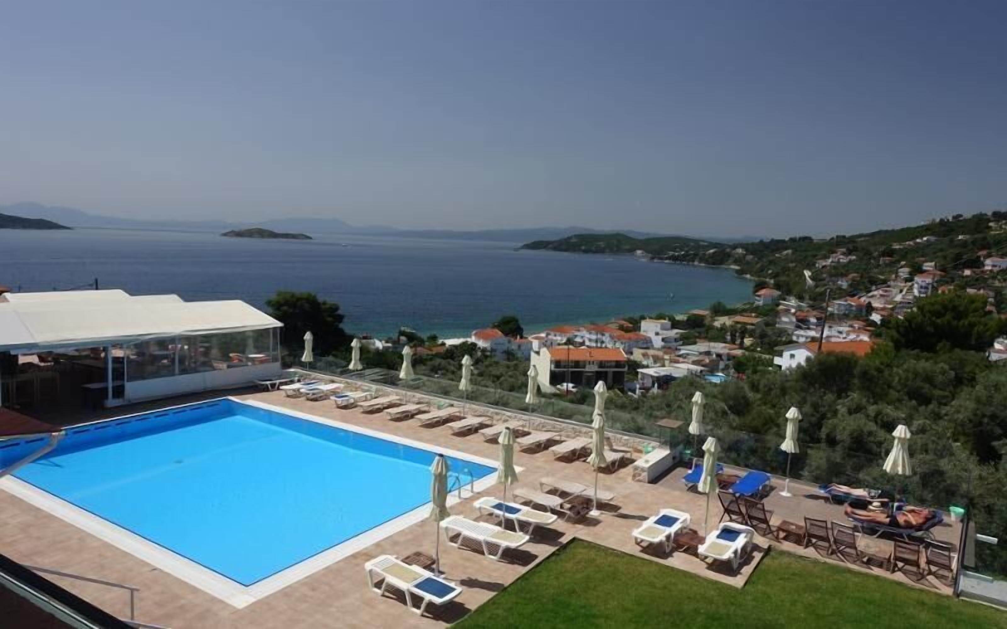 A pool area with lounge chairs and umbrellas, overlooking a coastal town and the sea.