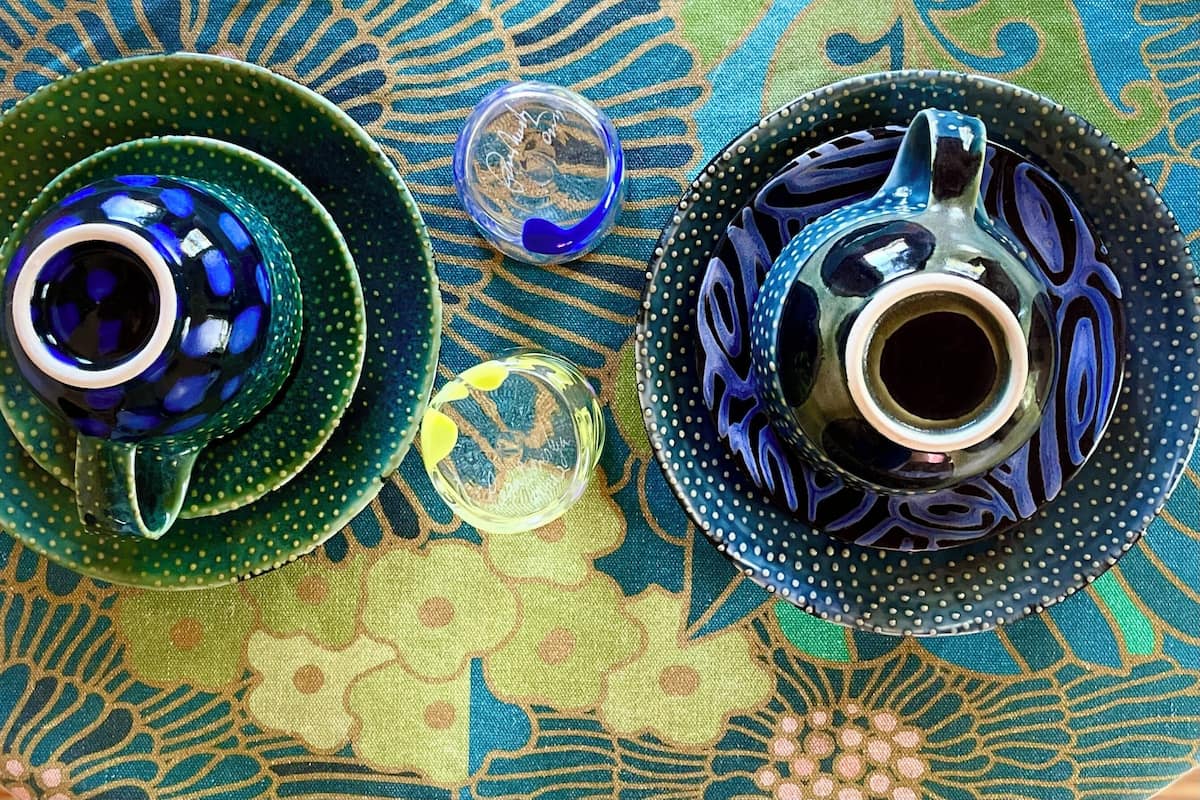 Due teiere in ceramica con coperchi su una tovaglia fantasia.