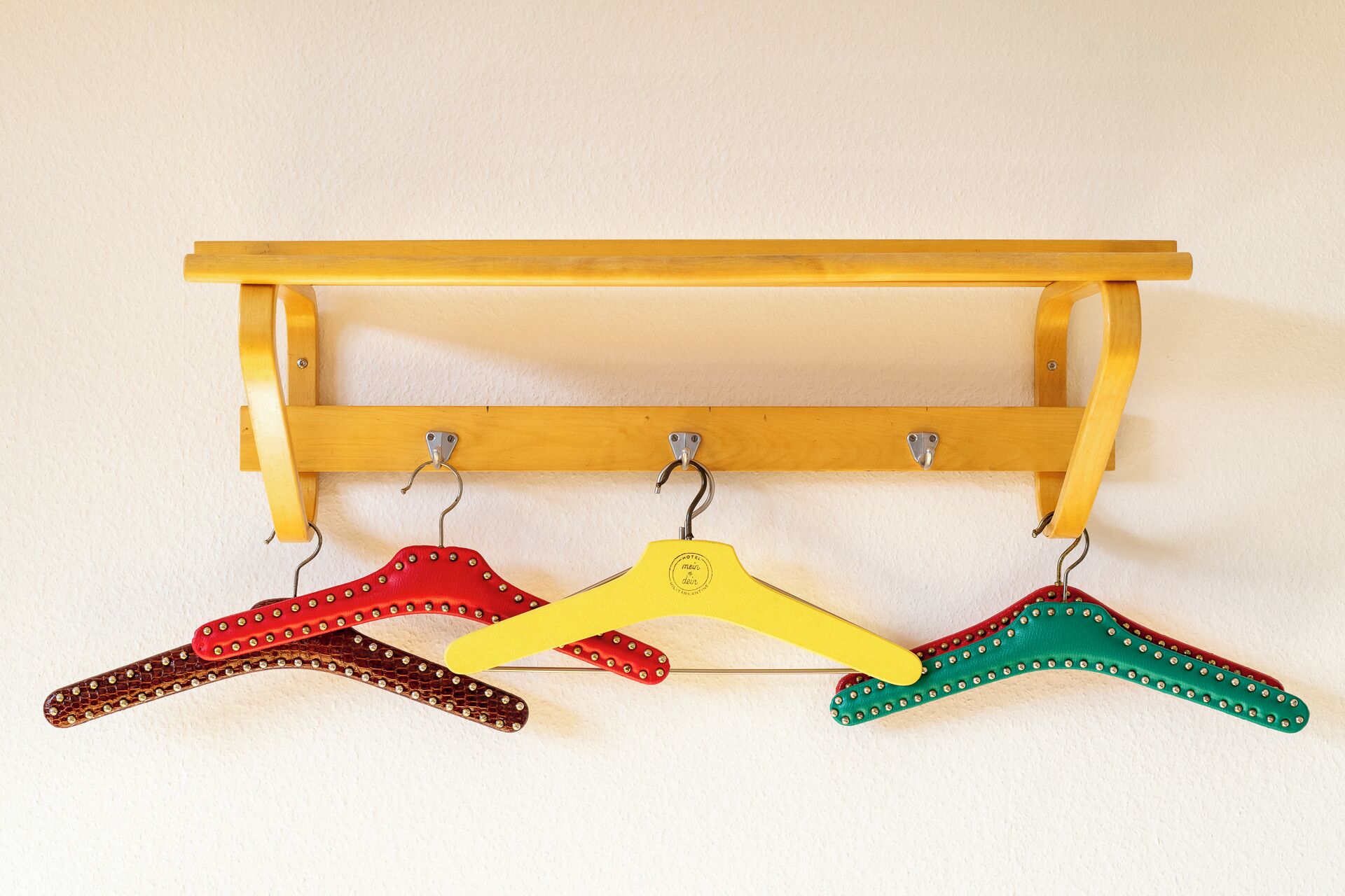 Un perchero de madera con tres colgadores, cada uno con diferente color y diseño.