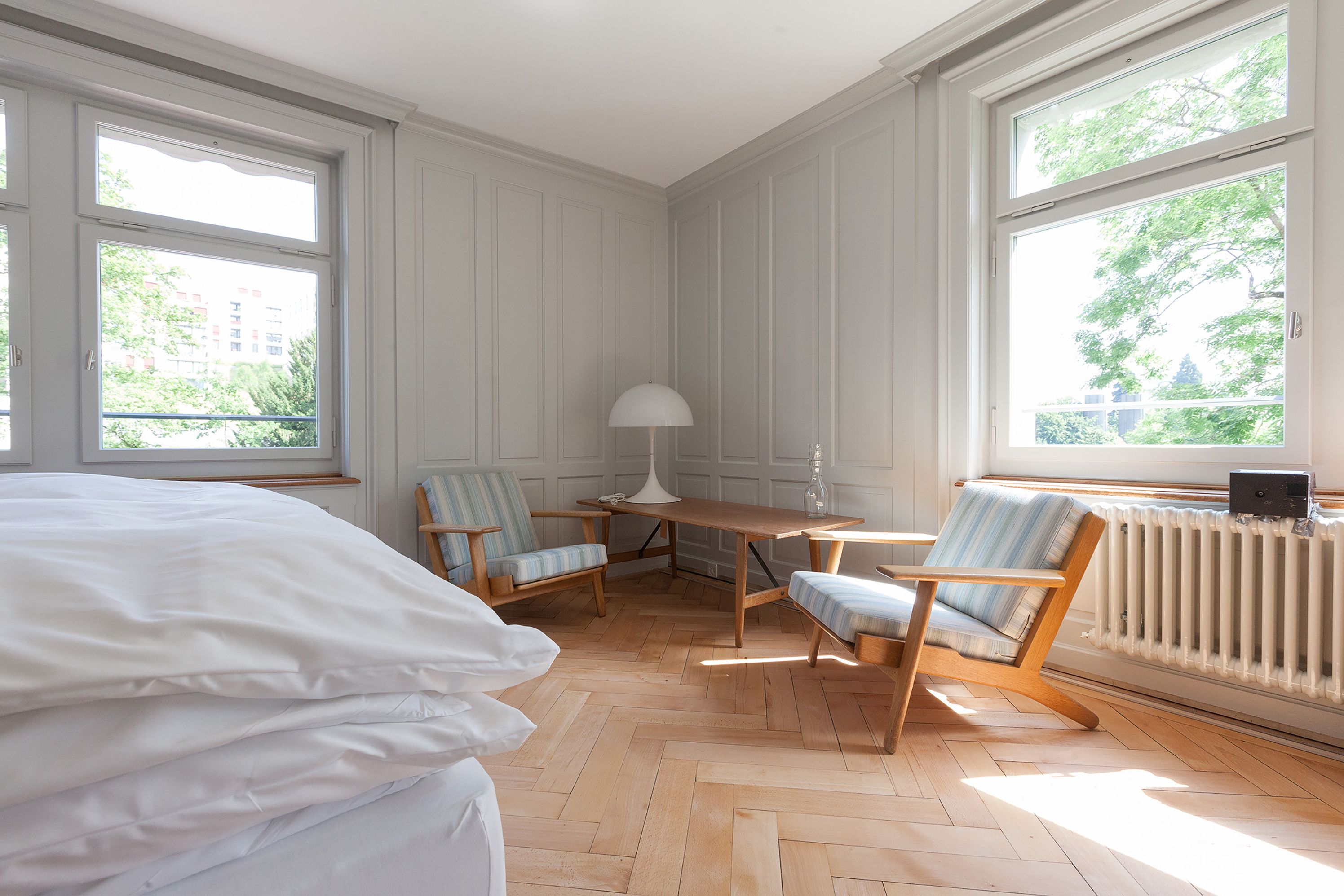 Una habitación con cama, mesa, dos sillas, lámpara y radiador.