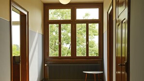 A room with a wooden herringbone floor, a radiator, a table, and a window with a view of trees. - Hotel Militärkantine (St. Gallen)