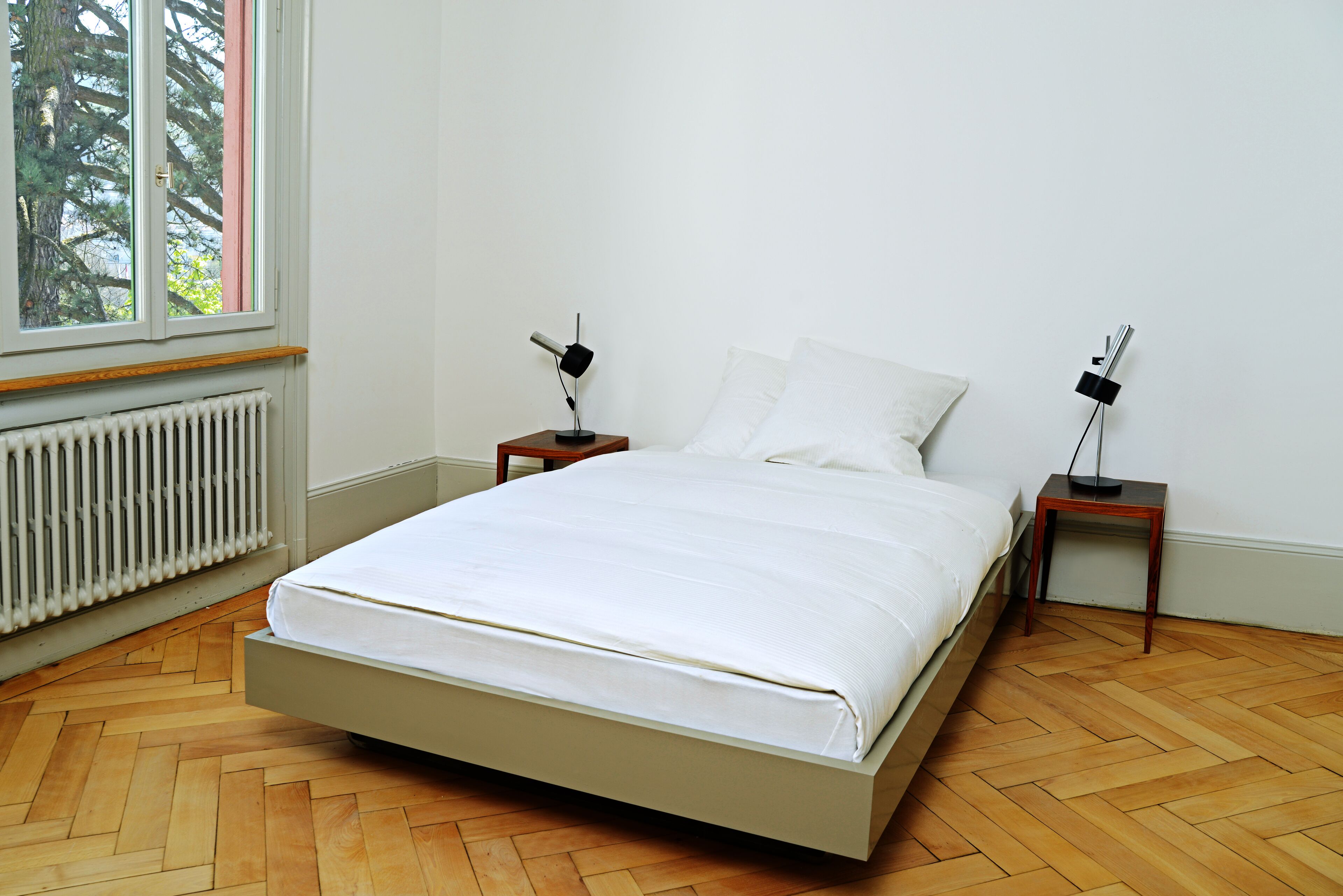 Ein Schlafzimmer mit einem Bett, zwei Nachttischen, einem Fenster und einer Heizung.