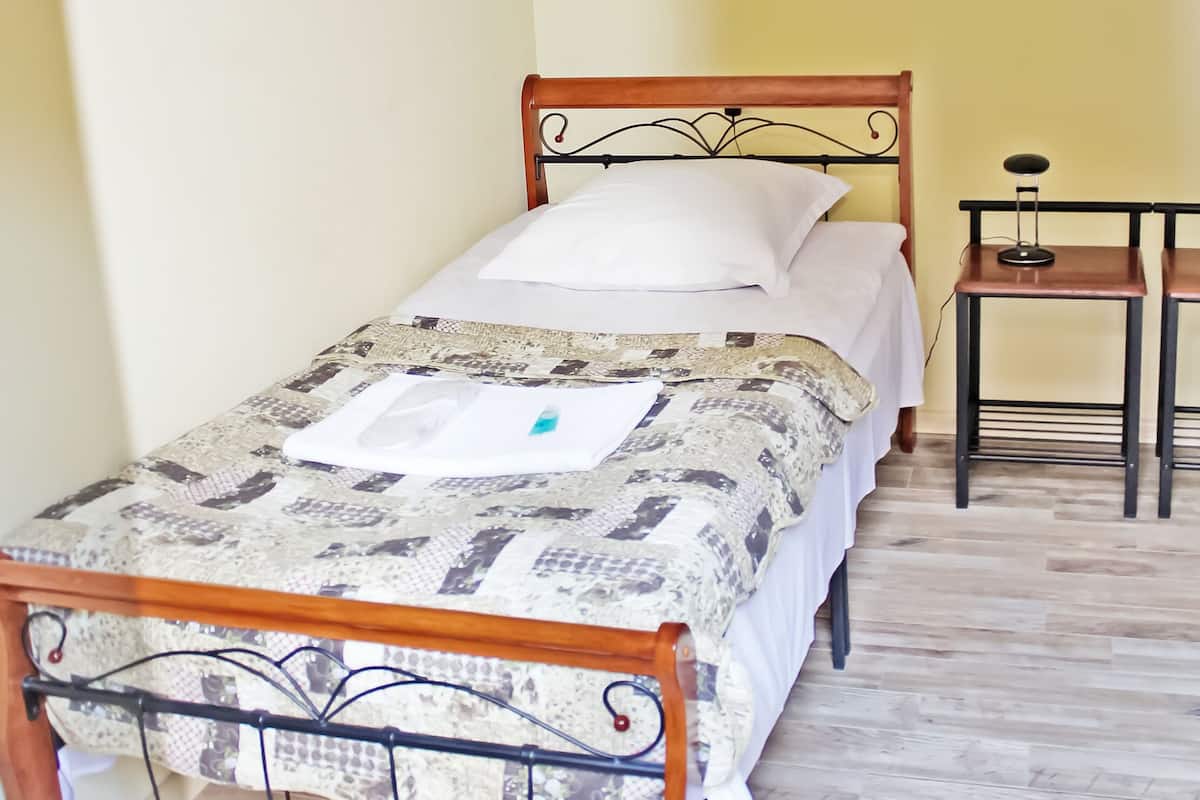 A twin bed with a patterned bedspread, a bedside table with a lamp, and a small table with a chair.