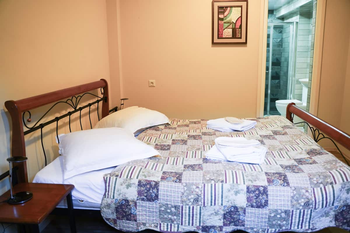 A neatly made bed with a quilt, a bedside table with a lamp, and a framed picture on the wall.