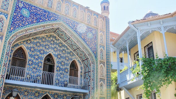 Un edificio con intrincados diseños de azulejos azules y blancos, ventanas arqueadas y un balcón con barandillas blancas.