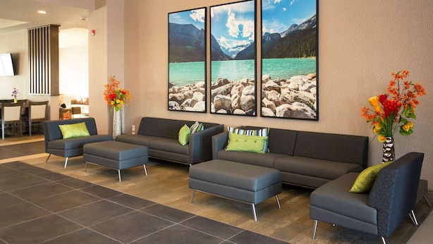 Un vestíbulo moderno con un sofá modular, dos sillones y una mesa de centro. Hay tres cuadros de paisajes enmarcados en la pared.