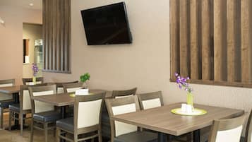 Un comedor con mesas y sillas de madera, un televisor de pantalla plana en la pared y jarrones decorativos con flores moradas.