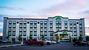 Un hotel Wingate con diseño moderno, que cuenta con un amplio estacionamiento y varios vehículos estacionados al frente.