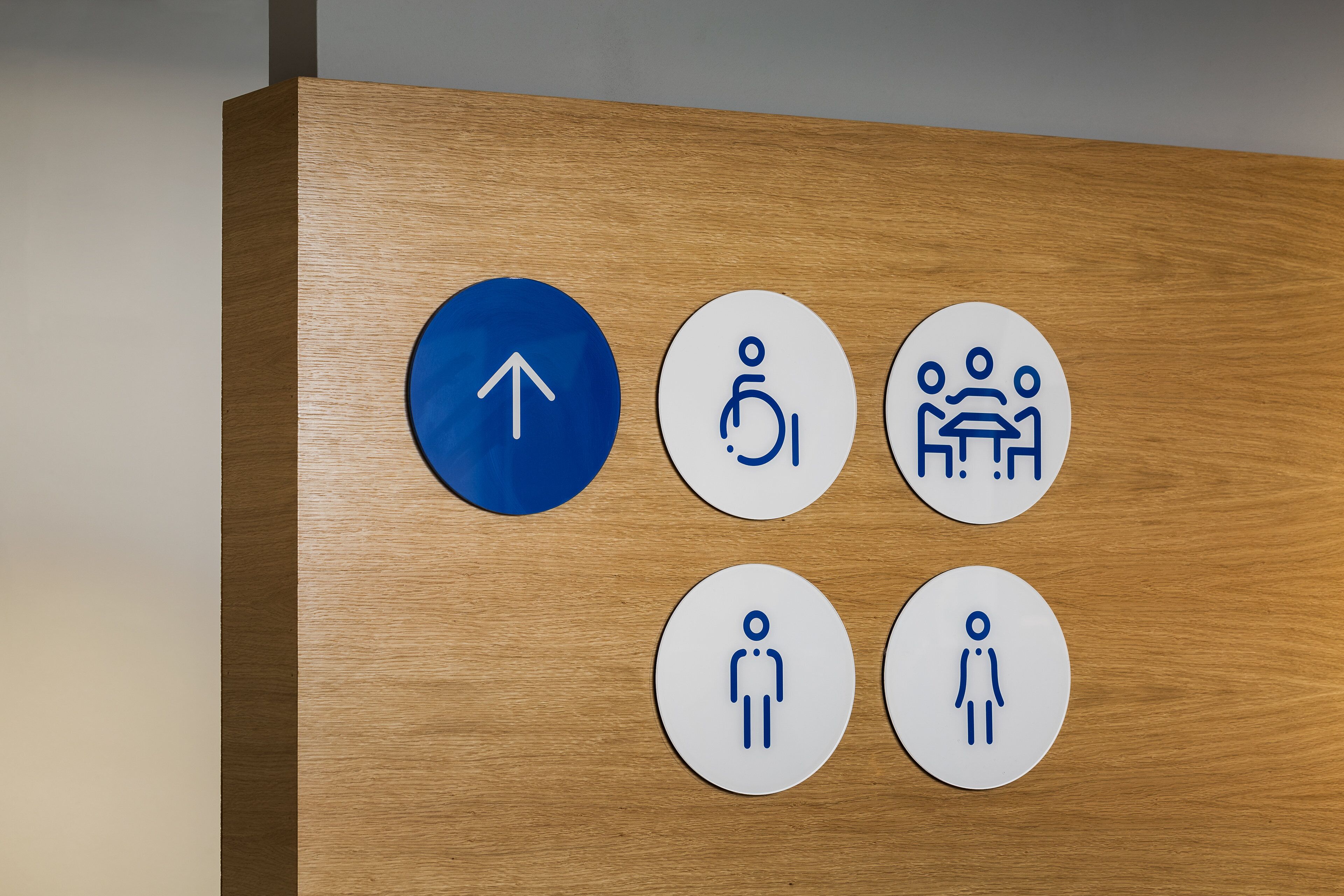 Painel de madeira com seis placas circulares indicando direções e comodidades.
