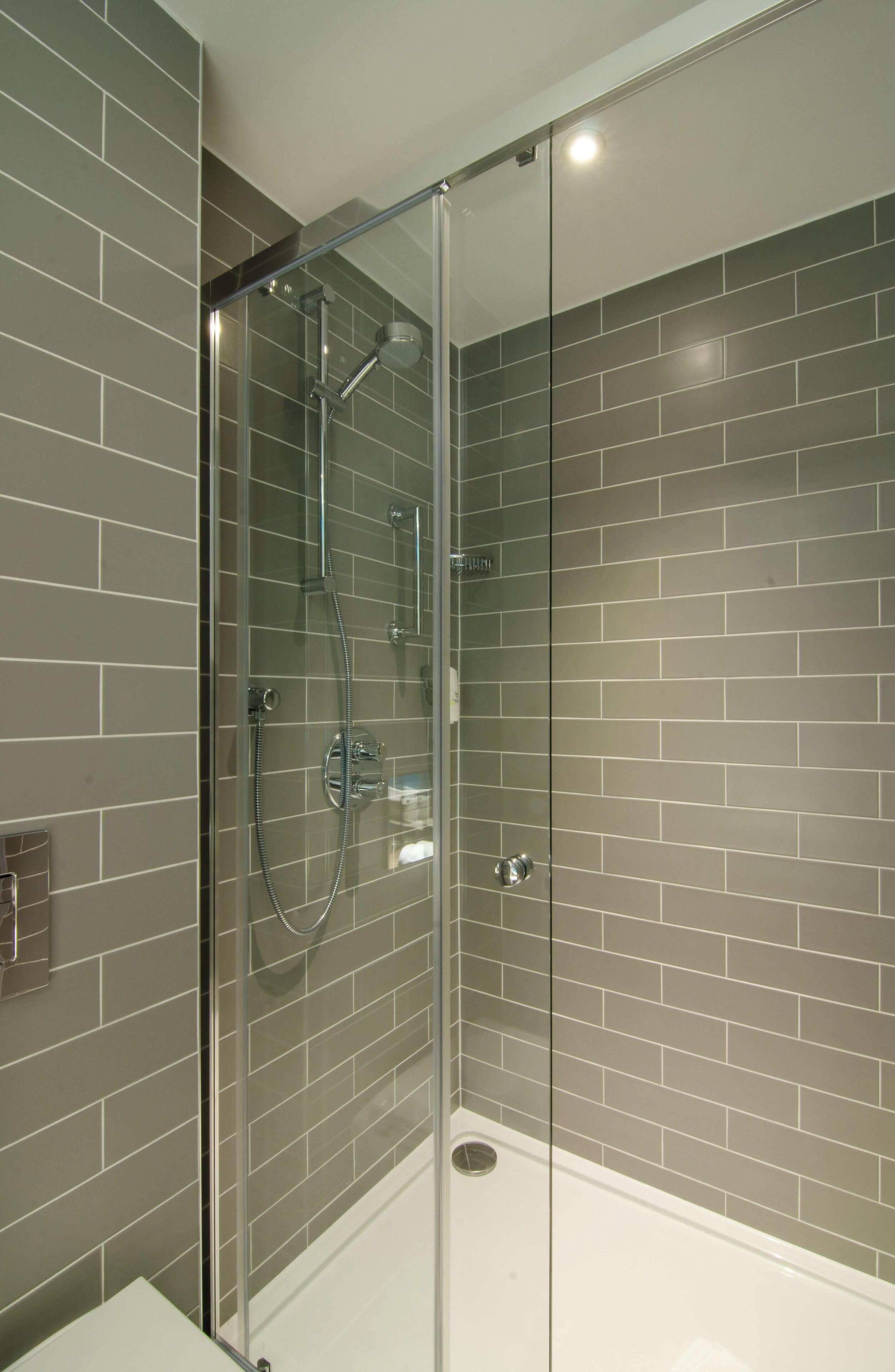 A glass-enclosed shower with a handheld showerhead and a wall-mounted faucet.