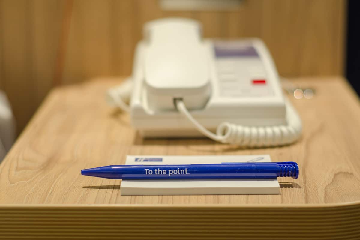 Een houten tafel met een witte telefoon en een blauwe pen op een vel papier.