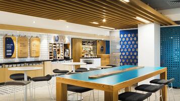 A modern bar area with wooden tables and chairs, a counter with a menu, and a decorative blue wall with circular patterns.