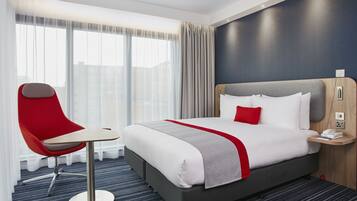 A hotel room with a large bed, a red chair, a small table, and a nightstand with a phone and a lamp.