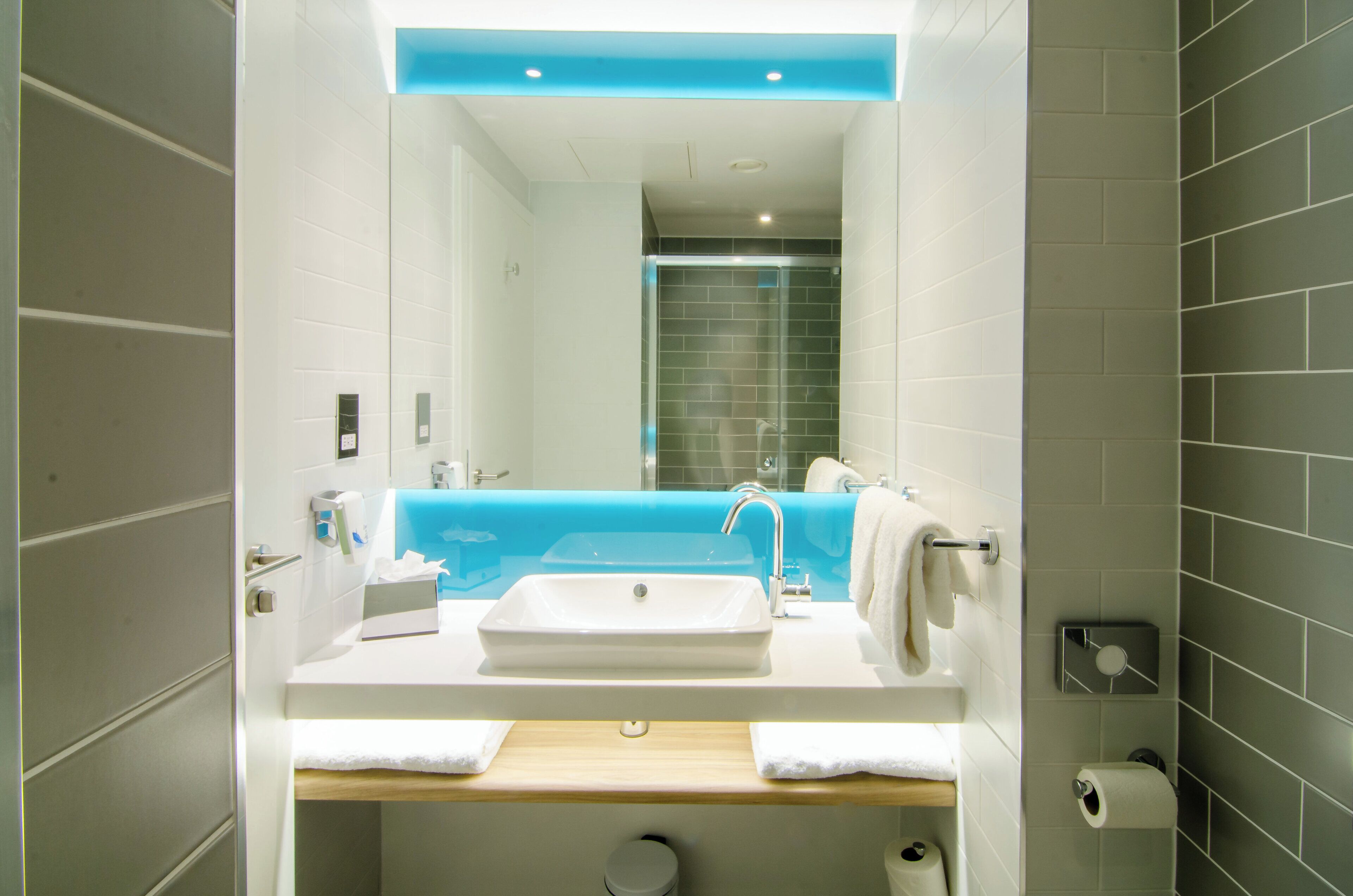 Un baño moderno con un lavamanos blanco, un espejo y una pared de acento azul.