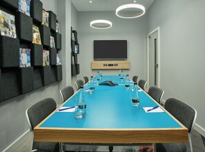 A conference room with a blue table, grey chairs, water bottles, and magazines on foam cubes. - Holiday Inn Express London - Ealing by IHG (London)