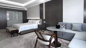 A modern hotel room with a bed, a sofa, a small table, and a chair. - Fenghua International Garden Hotel (Dongying)