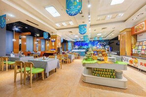 A restaurant interior with multiple dining tables, chairs, and a central display of food items. - Fenghua International Garden Hotel (Dongying)
