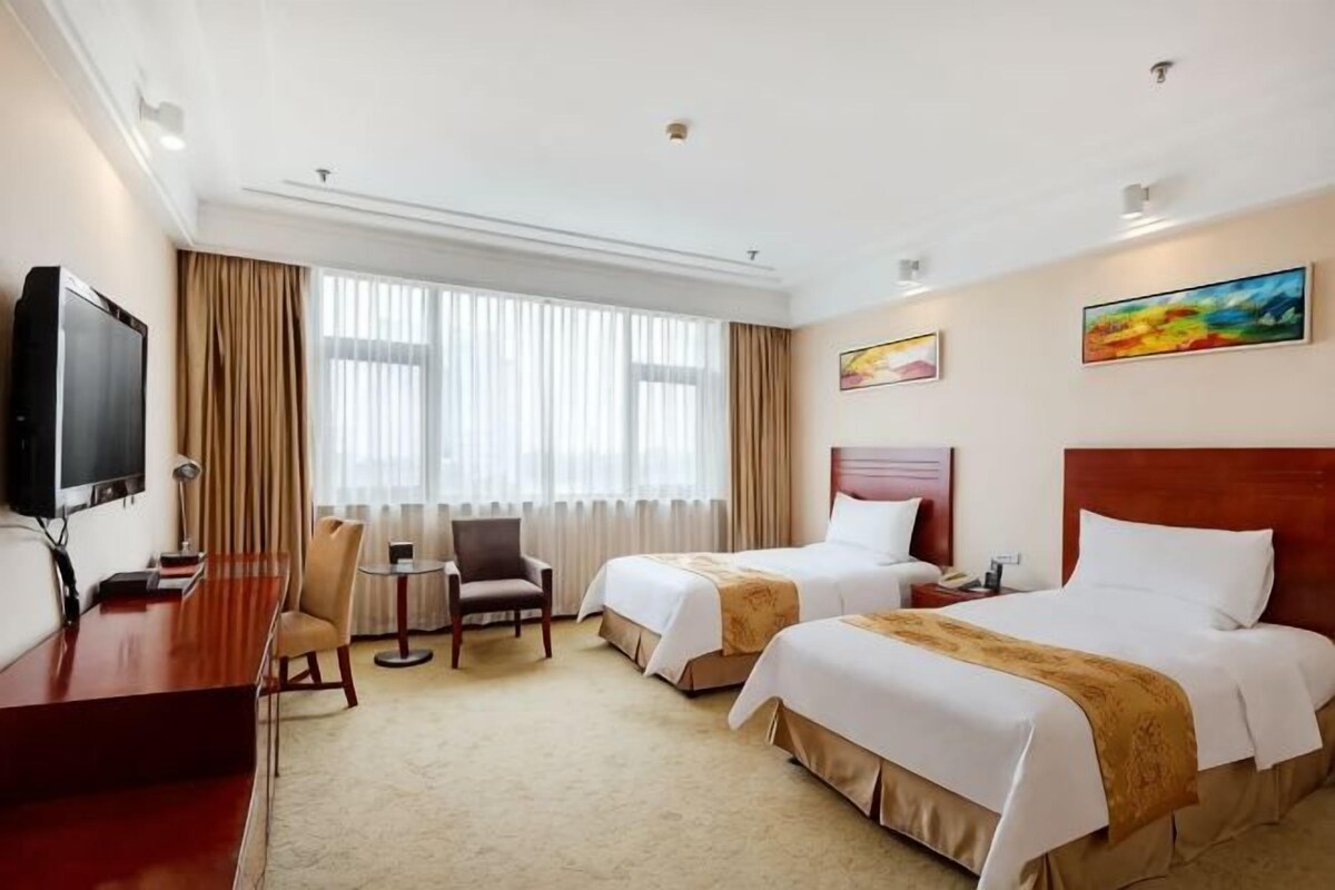A hotel room with two beds, a desk, a chair, a television, and a window with curtains.