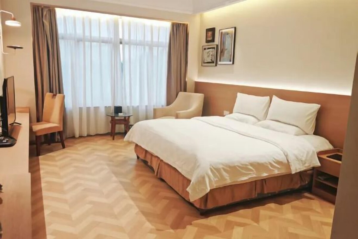 A hotel room with a large bed, two chairs, a TV, and a desk.