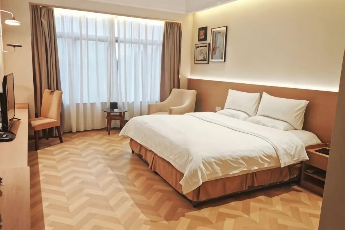 A hotel room with a large bed, two armchairs, a small table, and a TV.