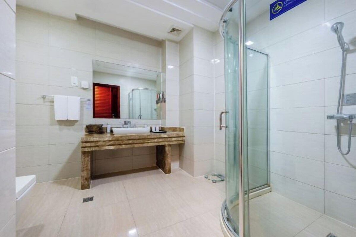 Un baño moderno con cabina de ducha de vidrio, tocador de mármol y un espejo grande.