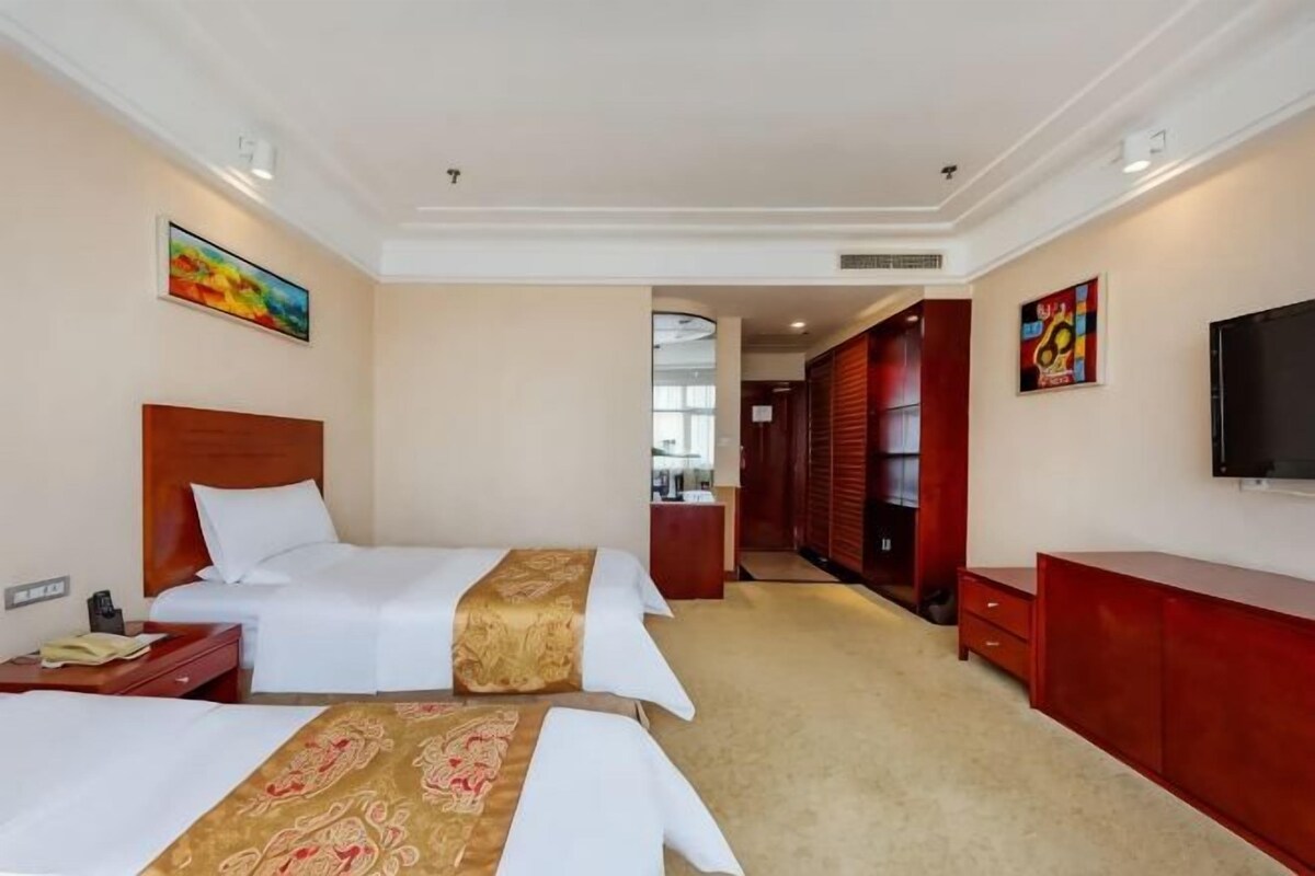 A hotel room with two beds, a desk, a TV, and a bathroom visible through a door.