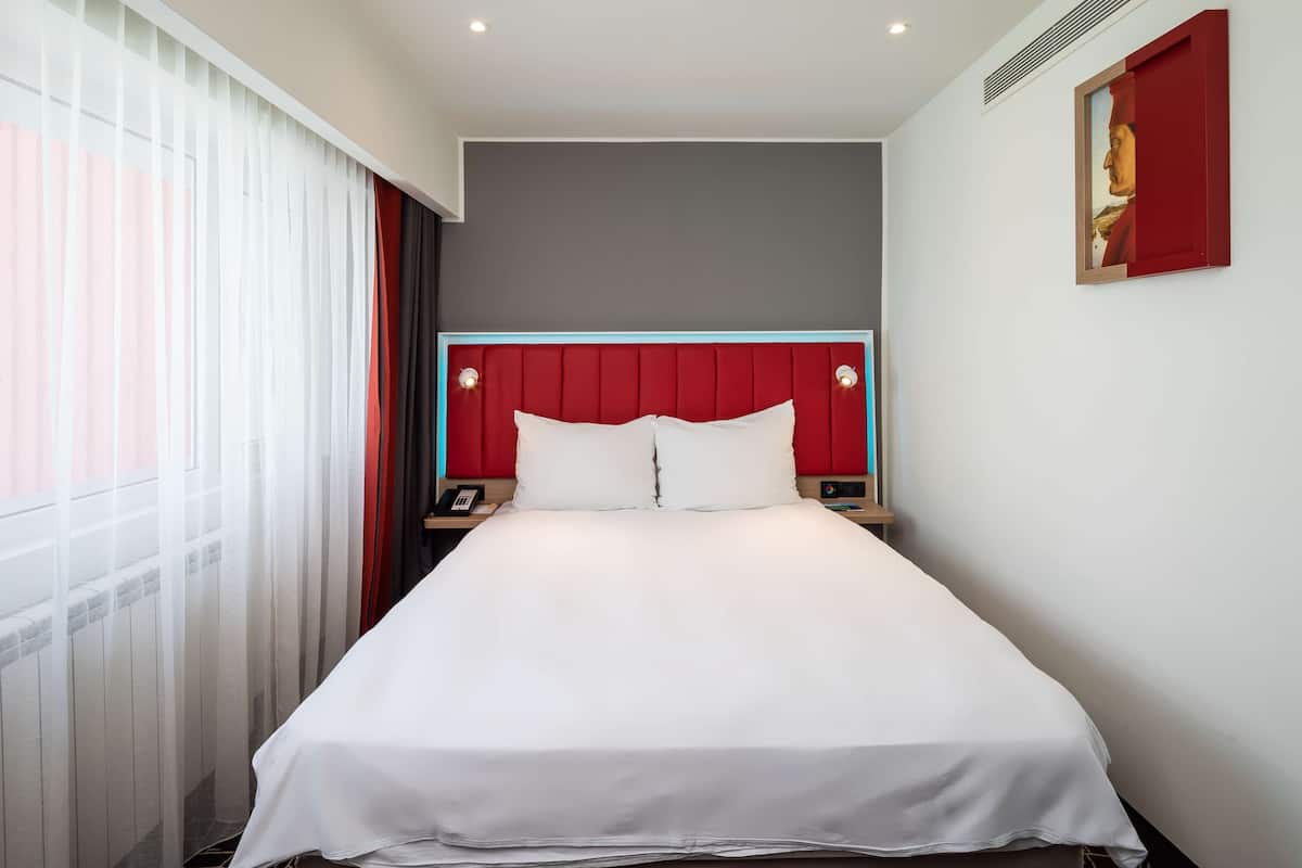 A hotel room with a large bed, a red headboard, and a nightstand with a phone.