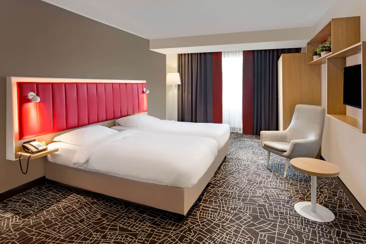 A hotel room with a large bed, a desk, a chair, and a TV.