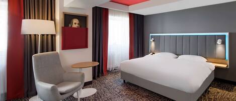 Une chambre d’hôtel avec un grand lit, un bureau, une chaise, une lampe et un tableau au mur.