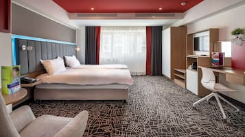 Habitación de hotel con dos camas, un escritorio, una silla, un televisor y un ventanal grande con cortinas.