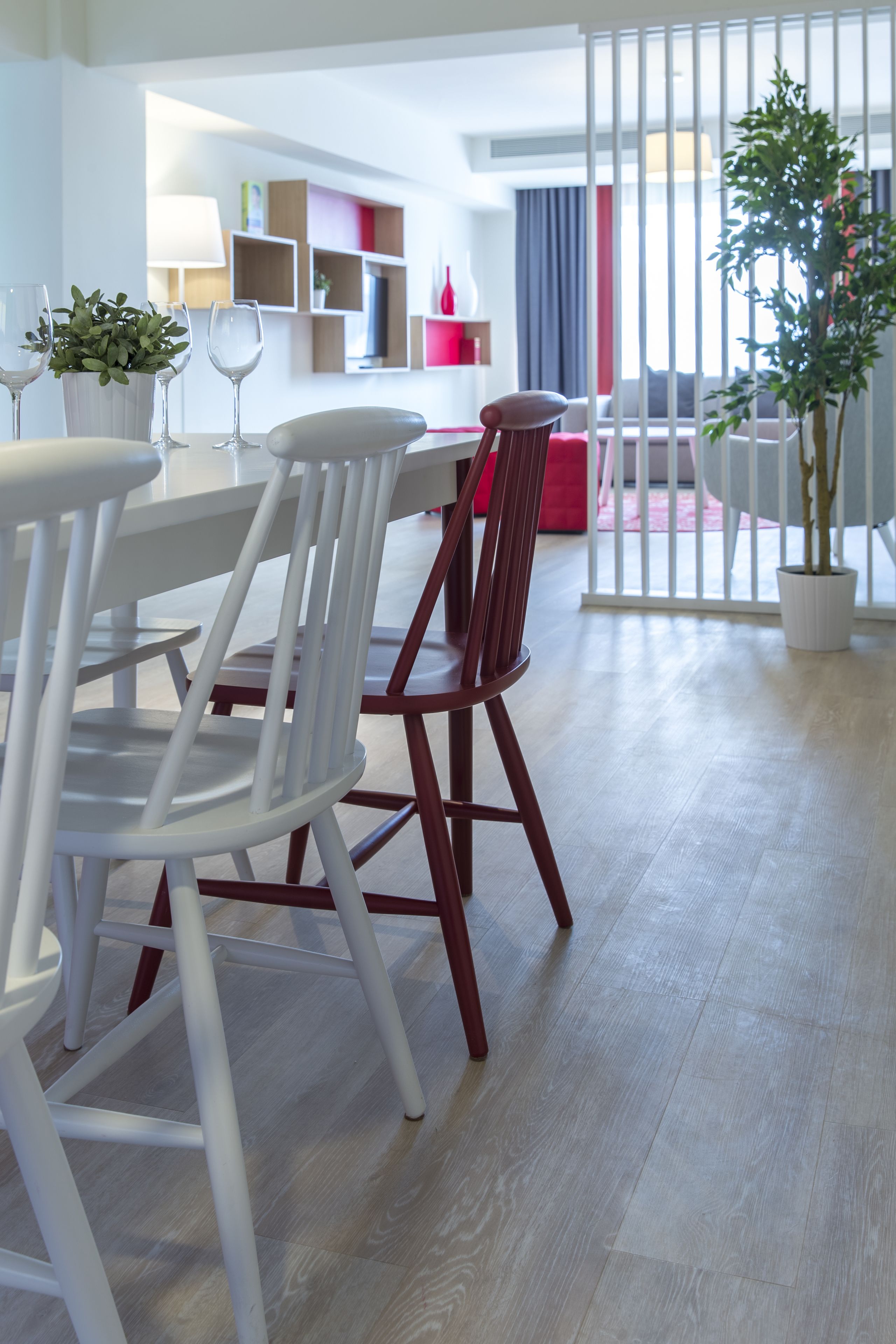 A modern dining area with white chairs and a wooden table, a red sofa, and a potted plant.