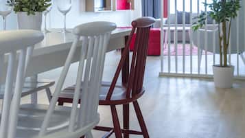 A modern dining area with white chairs and a wooden table, a red sofa, and a potted plant.