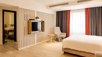 Une chambre d’hôtel avec un grand lit, un téléviseur fixé au mur, une petite table ronde, une chaise et une armoire.