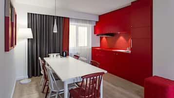 A modern kitchen with red cabinetry, a white dining table, and red chairs.