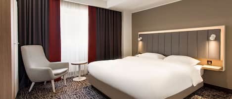 Una habitación de hotel con una cama grande, una silla, una mesita y una ventana con cortinas.