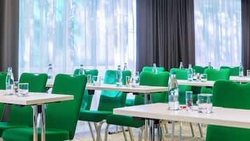Un salón de conferencias con sillas verdes y mesas blancas, cada una con botellas de agua y vasos.