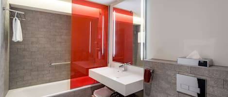 A modern bathroom with a white sink, a glass shower enclosure, and a red-tinted glass door.