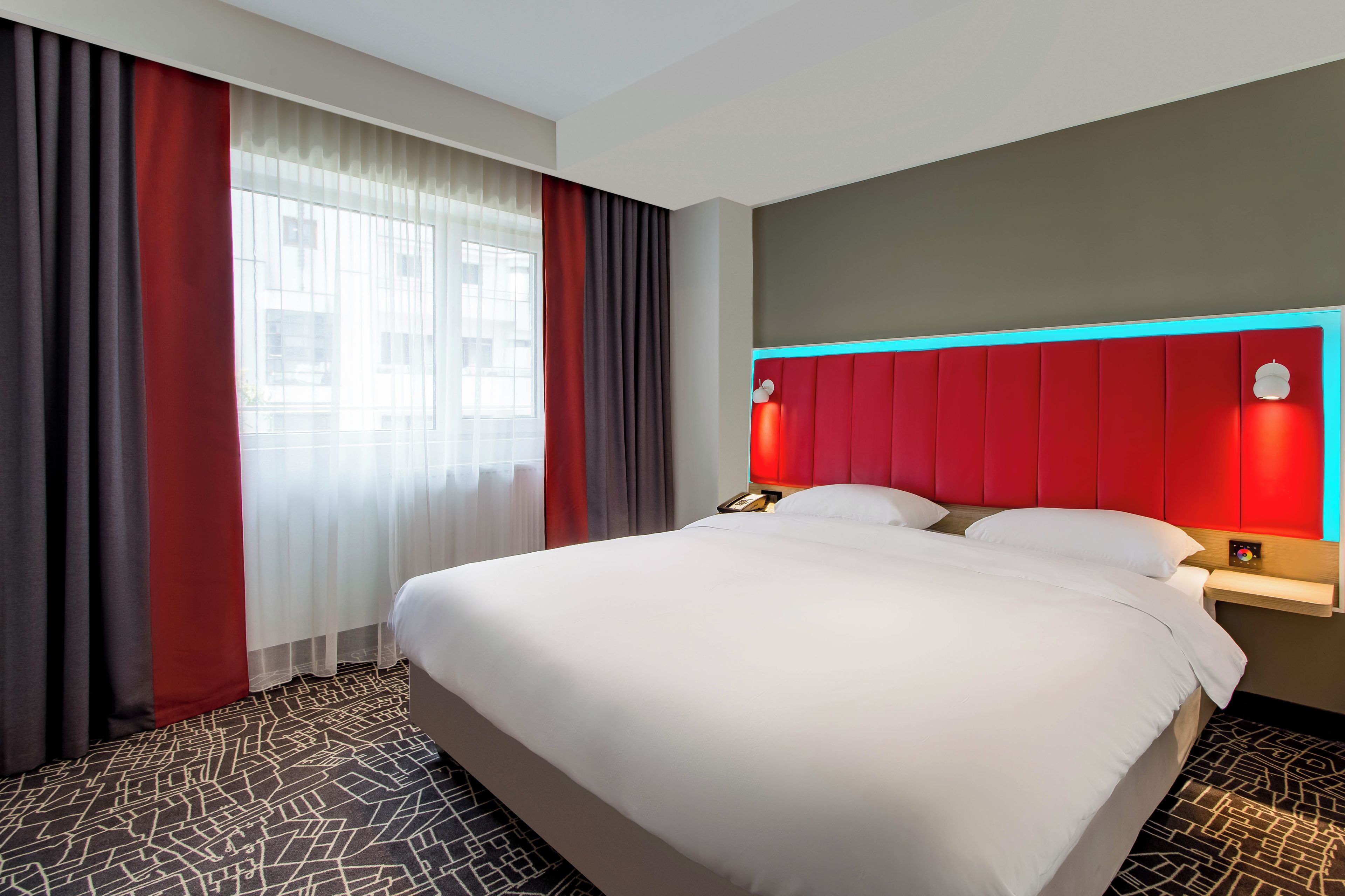 A hotel room with a large bed, a bedside table with a lamp, and a window with curtains.