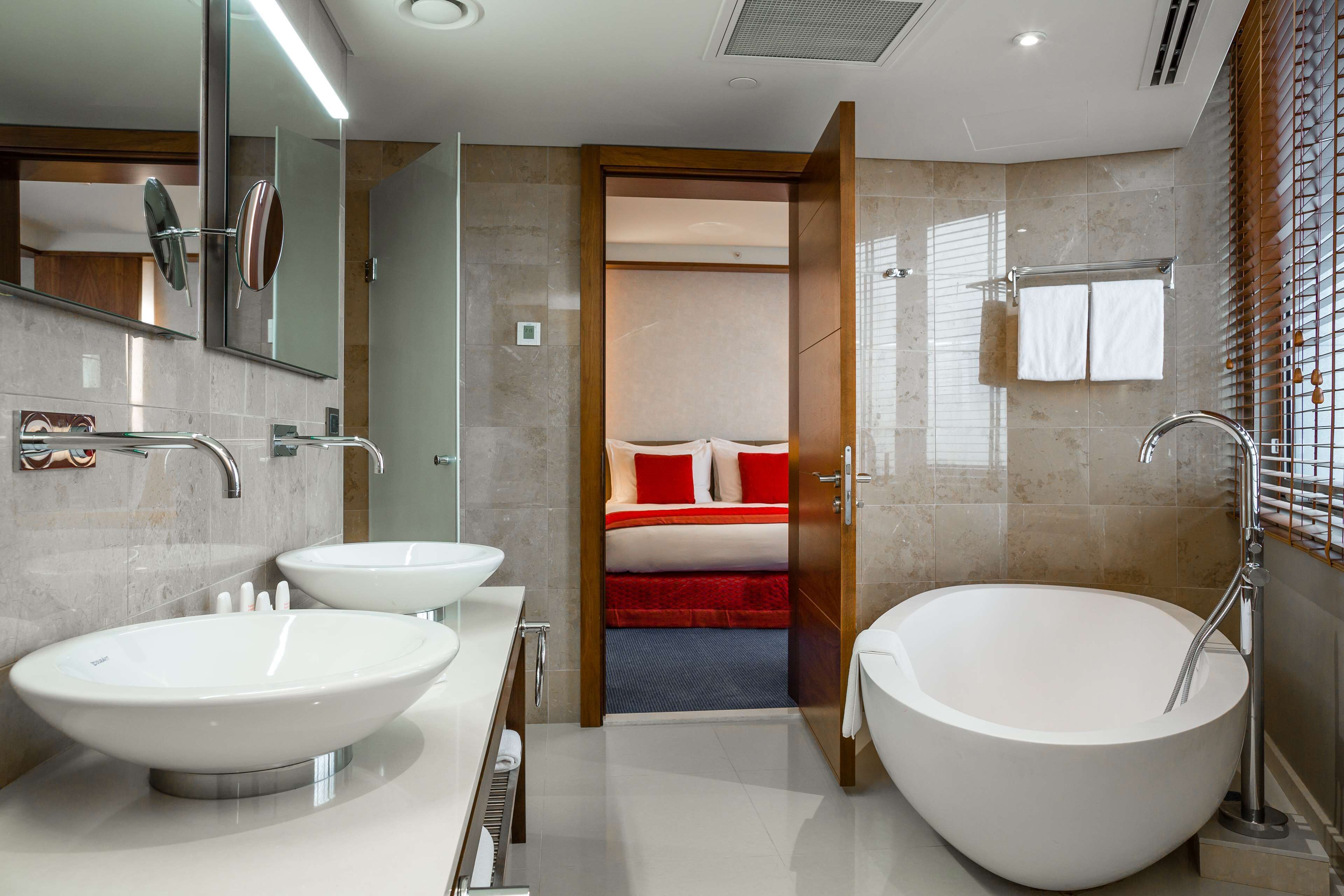 A modern bathroom with two large white sinks, a freestanding bathtub, and a mirror with a round frame.