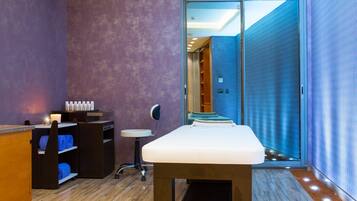 A room with a reception desk, a massage table, and a sliding glass door leading to a bathroom.