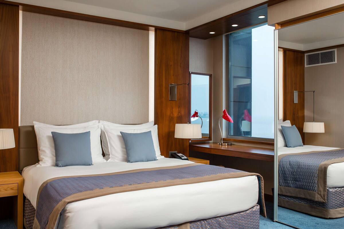 Une chambre d’hôtel avec un grand lit, un bureau avec une chaise, un miroir et une fenêtre.