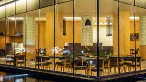 A modern restaurant with a glass enclosure, wooden paneling, and a dining area with tables and chairs. - Radisson Blu M'Bamou Palace Hotel (Brazzaville)