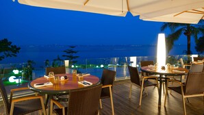 A dining area with a table and chairs, a large umbrella, and a view of the ocean at night. - Radisson Blu M'Bamou Palace Hotel (Brazzaville)