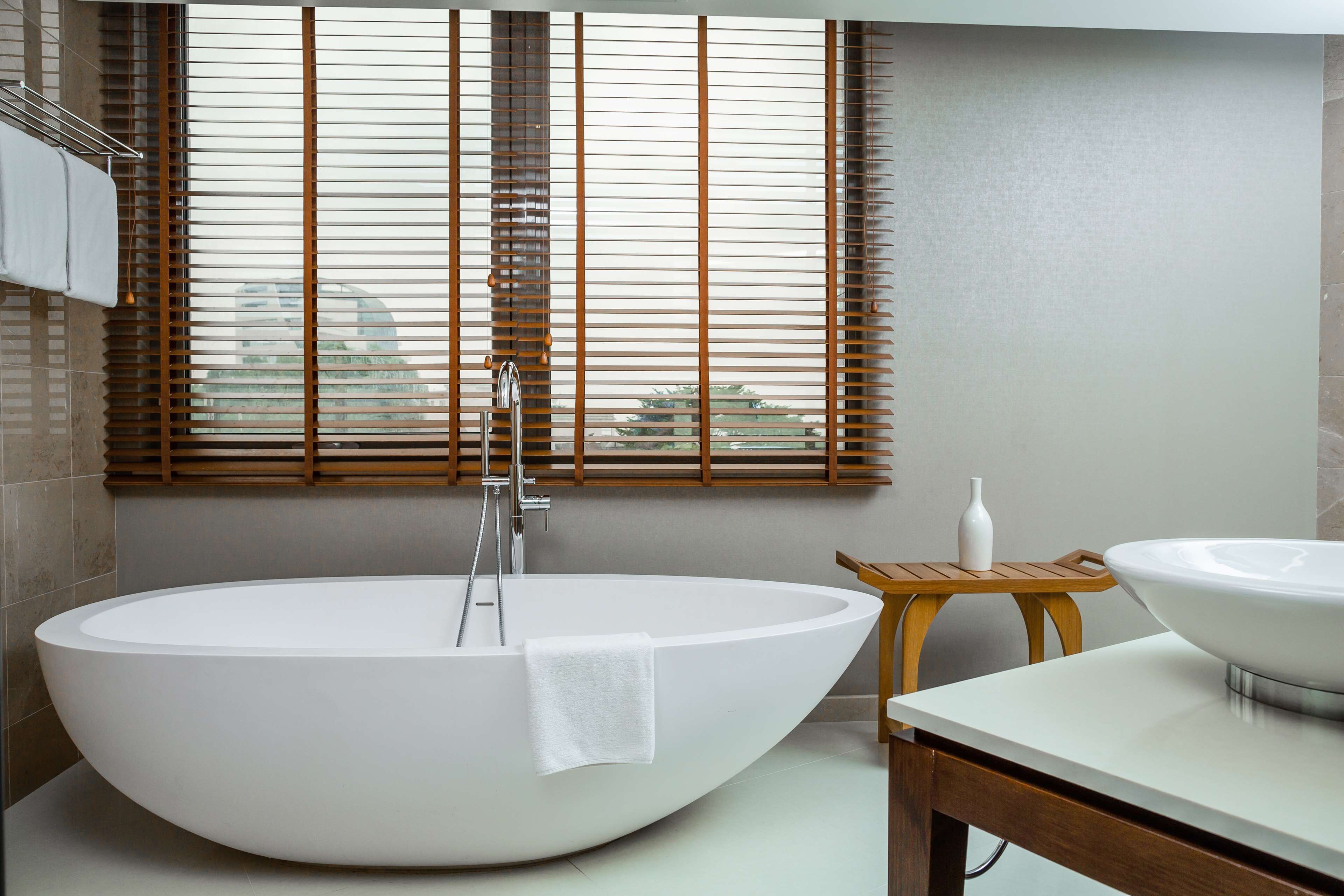 Un baño moderno con una bañera independiente, un tocador de madera y una ventana con persianas.